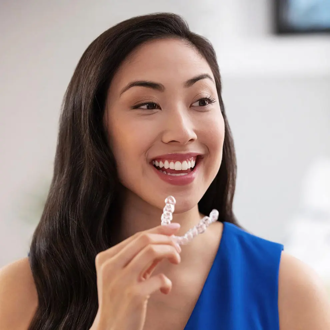 Paciente feliz segurando seu Mulher colocando alinhador transparente nos dentes, representando o início do tratamento ortodôntico estético. durante atendimento odontológico, reforçando os resultados estéticos do alinhamento dentário.