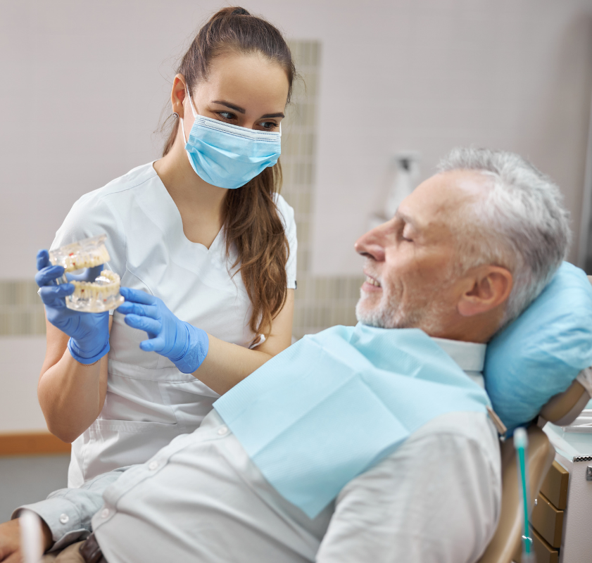 Dentista apresentando modelo de implante dentário a paciente idoso durante consulta, representando orientação personalizada no tratamento