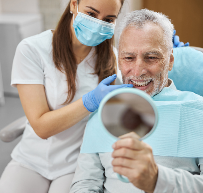 Paciente idoso sorrindo ao se ver no espelho após avaliação com dentista, simbolizando satisfação com o implante dentário