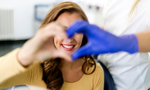 Paciente sorrindo enquanto forma um coração com as mãos junto à dentista, simbolizando confiança e satisfação com o atendimento odontológico.